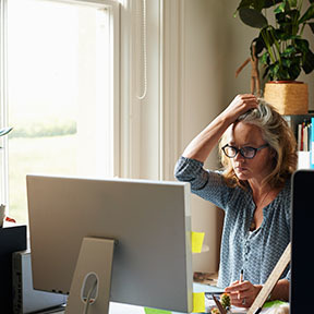 Woman sitting in front of computer next to window; she is clutching her hair with one hand